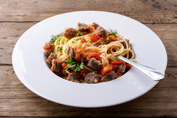 pasta with tomato sauce and meat on white plate and wooden background