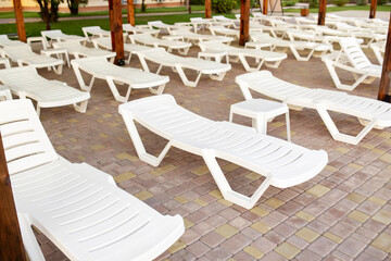 Empty white plastic loungers near the swimming pool on a summer day. Summer holidays and tourism. Relaxation area, place to rest
