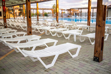 Empty white plastic loungers near the swimming pool on a summer day. Summer holidays and tourism. Relaxation area, place to rest