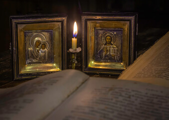 Icons of the Virgin Mary with the infant Christ and Nicholas the saint at a burning candle illuminating the opened sacred religious books