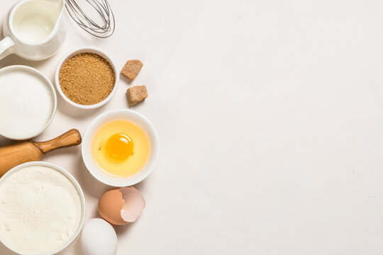Baking ingredients at white table. Flour, sugar, eggs and utensils. Top view with copy space.