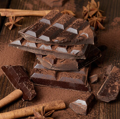 broken pieces of dark chocolate, cinnamon sticks and star anise on a brown wooden table, top view