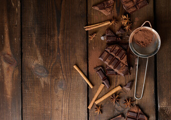 broken pieces of dark chocolate, cinnamon sticks and star anise on a brown wooden table, top view