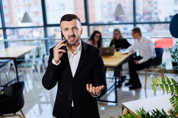 Handsome young businessman in modern suit using his mobile phone, successful man talking on the phone in the office