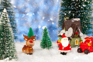 Toy santa claus and sleigh in the snow, artificial fir trees around, christmas greeting card