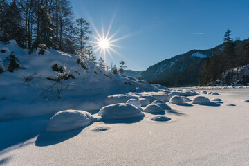 Weitsee zugefroren mit Schnee im Winter bei Sonnenschein mit Bergen und Wald im Gegenlicht mit Sonne