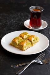 Pistachio baklava dessert on a dark background. Turkish sweet dessert concept. plate of pistachio baklava. sherbet sweet Mediterranean bakery. close up. selective focus.