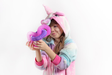 Cheerful little girl in unicorn pajamas plays in a popular toy poptube. An exciting children's game with multi-colored plastic pipes.