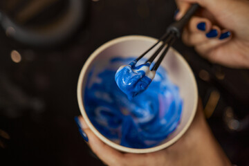 girl in white rubber protective gloves holding a brush in her hands and stirring hair dye close-up...