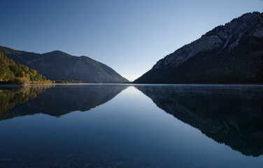 Alpiner Bergsee Plansee im morgendlichen Nebel an einem kalten Tag im Herbst mit Sonnenaufgang in...