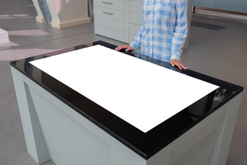 Woman in blue plaid shirt looking at blank interactive touchscreen white display of electronic table kiosk at exhibition or museum. White screen, mock up, copyspace, template, technology concept.