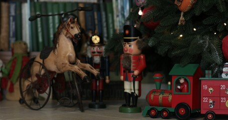 Advent calendar in shape of wooden red Santa train under Christmas tree decorated with retro Christmas ornaments. Antique nutcracker soldier toy and doll horse under artificial fir tree