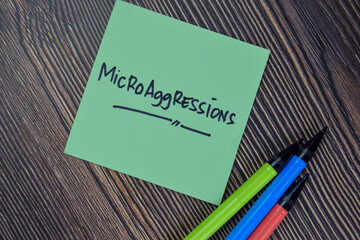 Microaggressions write on sticky notes isolated on Wooden Table.