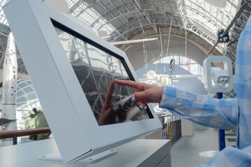 Close up: woman in blue plaid shirt touching interactive touchscreen display of electronic kiosk at futuristic exhibition or museum - scroll, touch gesture. Education, learning, technology concept