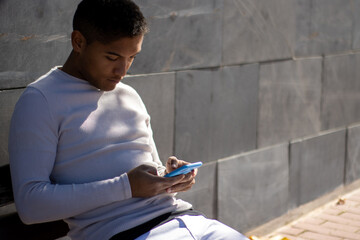 male person sitting on a bench looking at his mobile phone