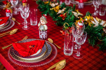 Wonderful table for the celebration of Christmas set up with plates, glasses, wine glasses, and golden cutlery with ornaments in red tones. Christmas ornaments on the table.