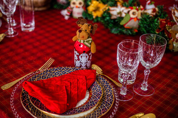 Wonderful table for the celebration of Christmas set up with plates, glasses, wine glasses, and golden cutlery with ornaments in red tones. Christmas ornaments on the table.