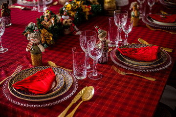Wonderful table for the celebration of Christmas set up with plates, glasses, wine glasses, and golden cutlery with ornaments in red tones. Christmas ornaments on the table.