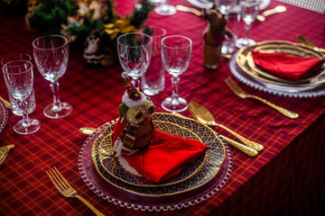Wonderful table for the celebration of Christmas set up with plates, glasses, wine glasses, and golden cutlery with ornaments in red tones. Christmas ornaments on the table.