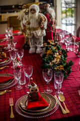 Wonderful table for the celebration of Christmas set up with plates, glasses, wine glasses, and golden cutlery with ornaments in red tones. Christmas ornaments on the table.