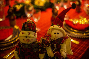 Wonderful table for the celebration of Christmas set up with plates, glasses, wine glasses, and golden cutlery with ornaments in red tones. Christmas ornaments on the table.