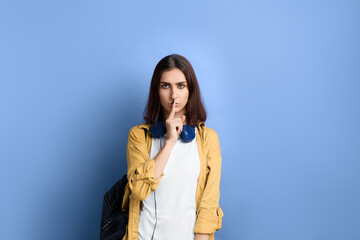Keep silence please. Serious student girl is asking to be quiet, keeps index finger over lips,...