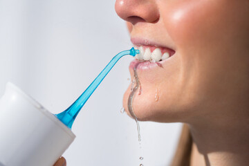 Woman with perfect white smile using portable water flosser or oral irrigator