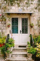 Fototapeta na wymiar Threshold of an old stone house with a wooden door with a forged lattice and flowers in pots