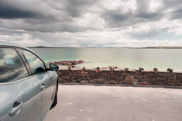 Car parked by the ocean. Beautiful nature scenery. Vast ocean surface, low cloudy sky. West of Ireland.