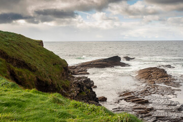 Green grass fields by the ocean and rough stone coastline, low cloudy sky. West coast of Ireland. Irish landscape. Nobody.