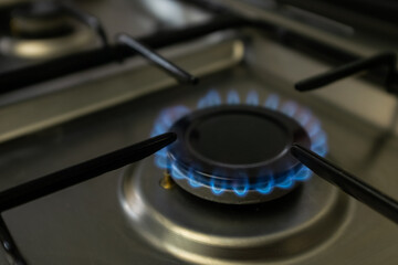 blue gas burning from kitchen gas stove. Gray metal surface with black grill.