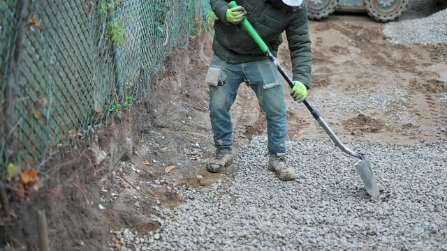 Demolition worker wearing hard hat using a shovel to ensure stones are level on driveway