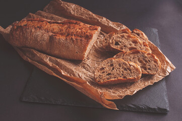Rustic bread, beautiful golden crust, sliced bread lying on black board