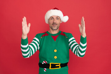 amazed man in elf costume. xmas guy in santa claus hat on red background. happy new year.