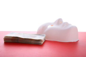 Mask and pile of money on a red table .