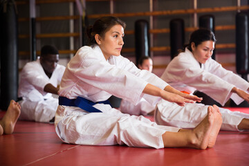 People in kimono warming up before karate training. They're doing stretching exercises for legs