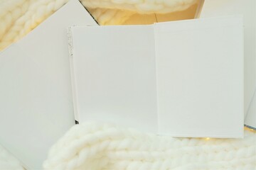 Winter books. Winter cozy reading. white books with blank sheets with white knitted scarf and garland.Cozy mood. Winter Season Christmas books.
