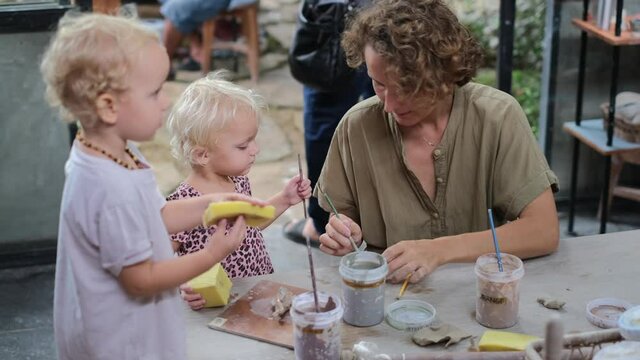 Young mother together with toddler twins on pottery workshop, art school for small kids, family leisure activity 