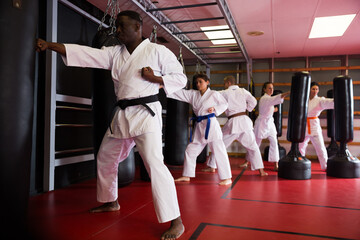 African american man in kimono practicing powerful body punches on heavy punchbag in gym