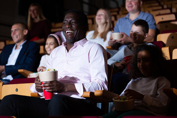 Portrait of cheerful laughing african american man sitting in movie theater with popcorn and...