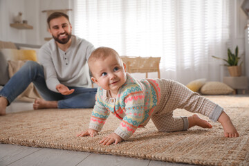 Happy young father watching his cute baby crawl on floor at home