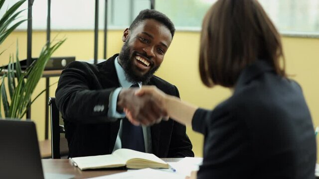 Young businessman talking to woman and shaking hand while sitting at table in company spbi. Close-up view of American African man talks to female colleague or partner and shakes arm, laughs and sits