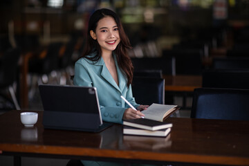 Portrait of Smiling a beautiful young Asian businesswoman sitting with laptop and computer while doing some paperwork at the out office. 