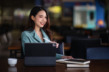 Portrait of Smiling a beautiful young Asian businesswoman sitting with laptop and computer while doing some paperwork at the out office. 