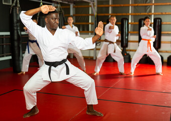 Fototapeta premium African-american man in kimono standing in fight stance during group karate training.