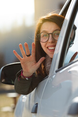 Naklejka premium Young woman in car waving out out of the window