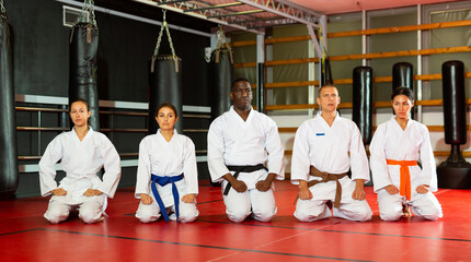 Group of athletes in kimono sit on a tatami before preparing for sparring