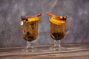 Two glasses of herbal tea with cinnamon and citrus fruits on a wooden table.