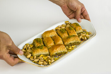 Hand carries A Tray Of Traditional Turkish Dry Baklava with pistachios on white surface