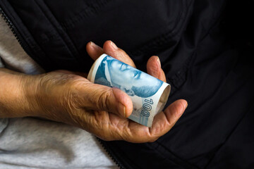 One hundred Turkish Lira rolled-up in the hand of an old person